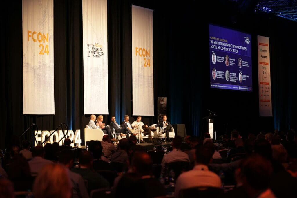 Panel discussion on stage at the 2024 Future of Construction Summit, with FCON24 banners and a seated audience