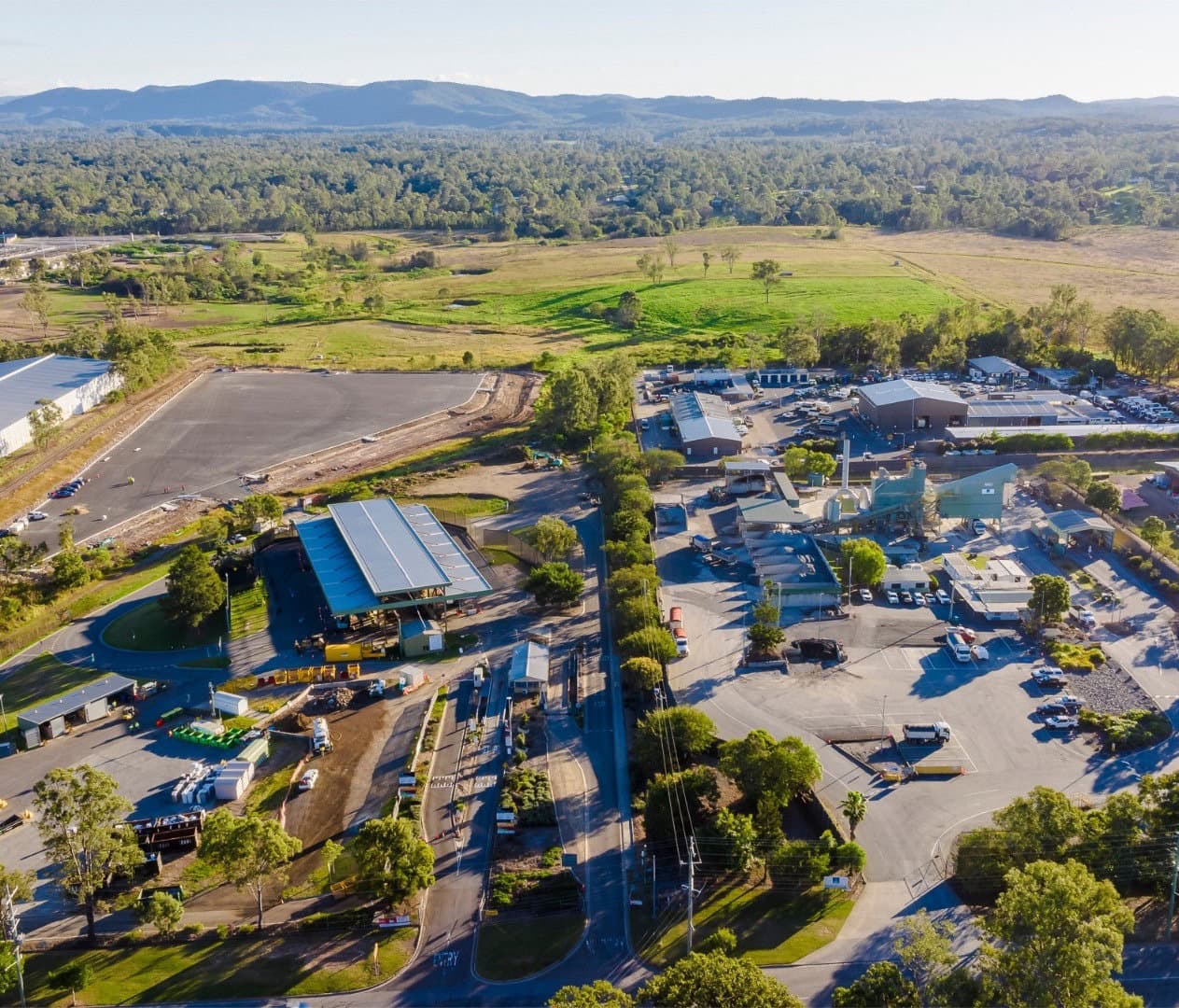 Aerial of the Riverview Waste and Resource Facility showing the processing buildings, weighbridge canopy, paved storage yards, and surrounding green pastures with distant mountains