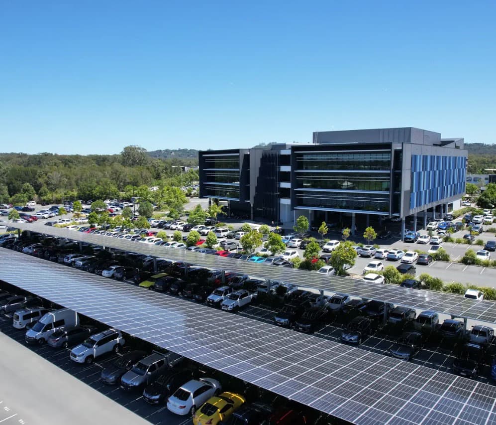 Aerial photograph of an S-Rack solar carport array covering a corporate car park, with the office building behind under a clear blue sky