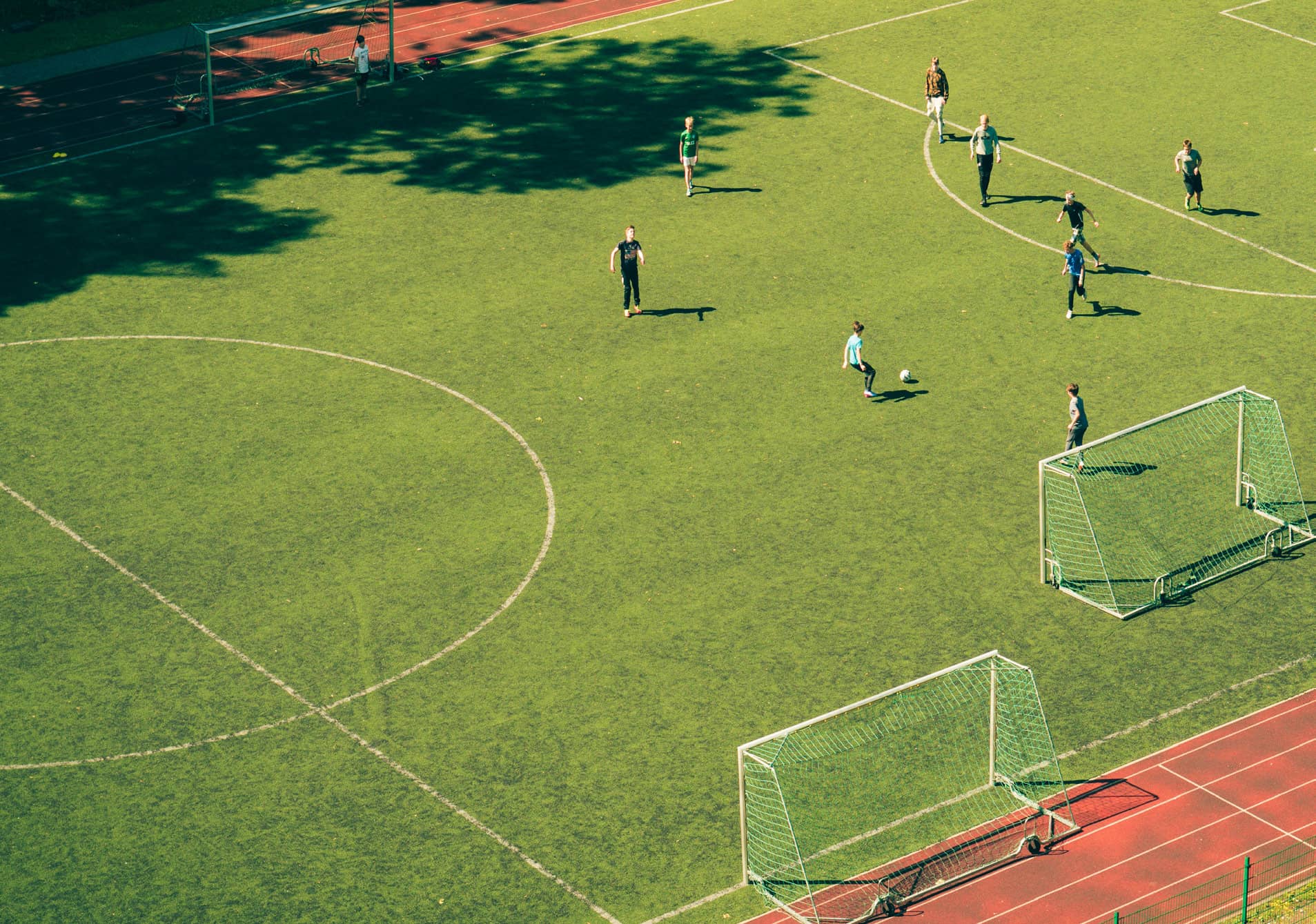 Aerial view of a community sports field with people playing soccer alongside an athletics running track